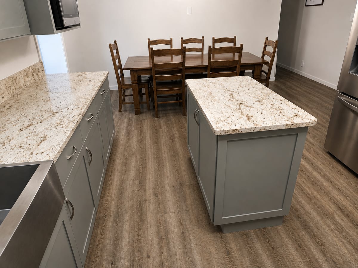 Gray shaker kitchen island with a light granite top next to a farmhouse dining table