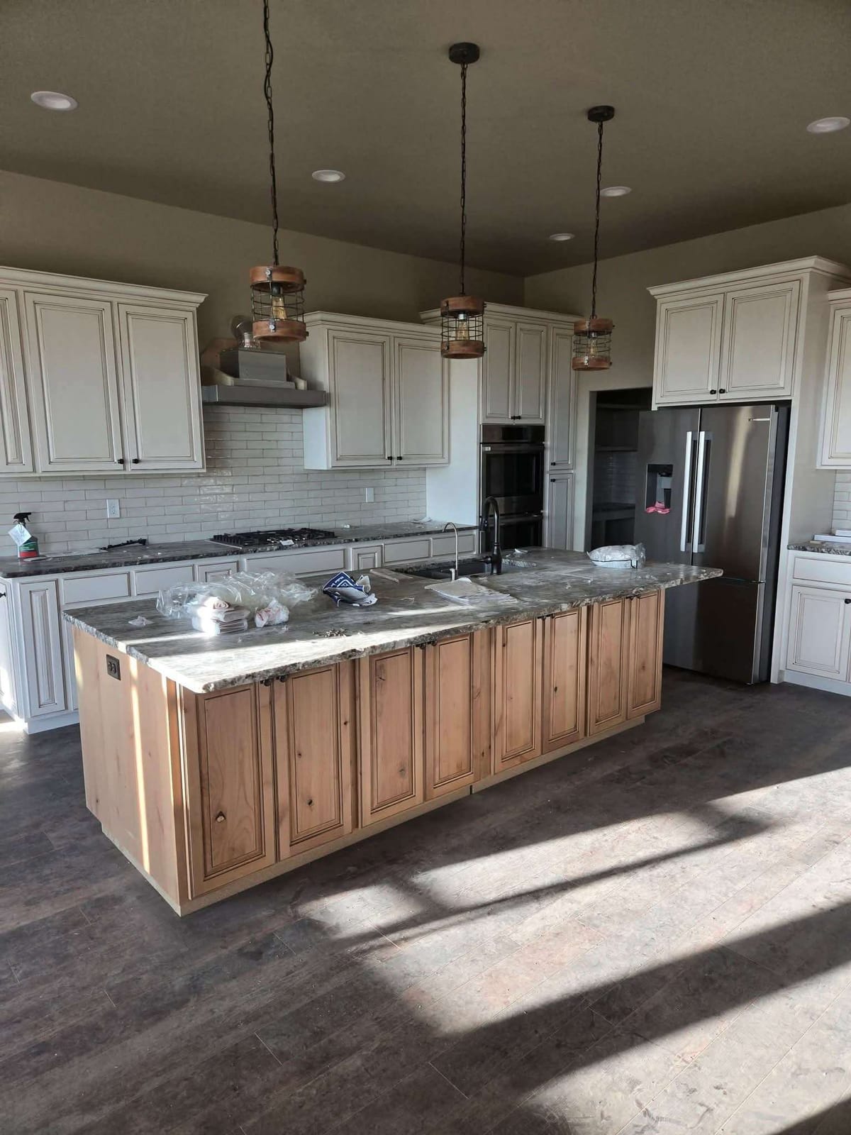 Knotty alder kitchen island with granite countertop and glazed cream perimeter cabinets in a new build