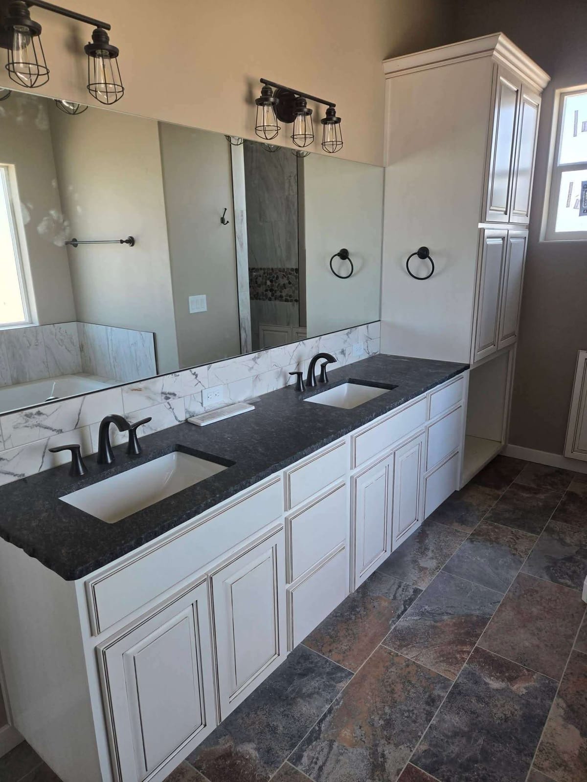 Custom double sink bathroom vanity with glazed white cabinets, dark granite top, and a linen tower